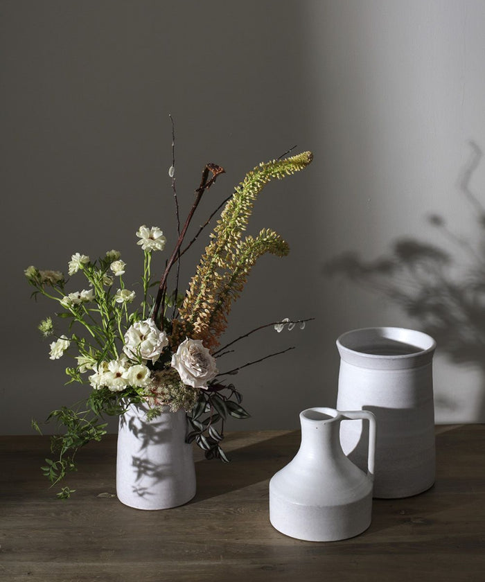 Three minimalist terracotta vases with a white matte finish of varying heights and shapes, conveying simplicity and elegance styled with a neutral floral arrangement. | Wildwood Home Co.
