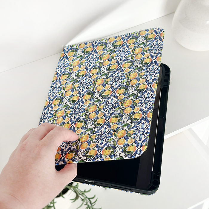 Hand opening a Coconut Lane iPad case in blue geometric vegan leather, shown against a white background.