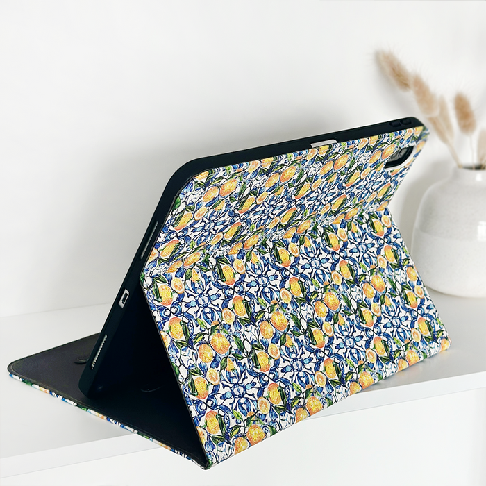 IPad in a yellow lemon-patterned Coconut Lane case on a white surface beside a vase of dried grass.