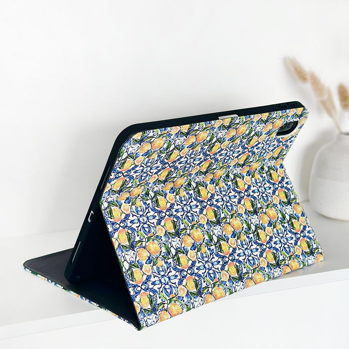 IPad in a lemon-patterned Coconut Lane case next to a white ceramic vase with dried flowers on a white surface.