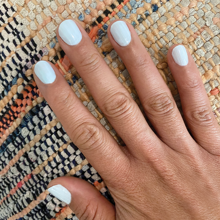 Hand displaying a smooth manicure with pale sky blue Angelfish gel polish on textured fabric background