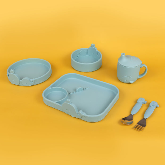The Animal Friends 6-Piece Dinnerware Set - Blue Whale is a light blue silicone baby feeding set with animal designs, including a plate, bowl, snack bowl, sippy cup, fork, and spoon—shown on a yellow background.