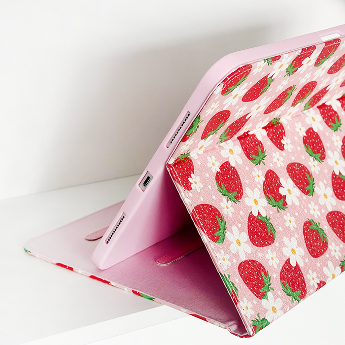 Pink tablet in a Coconut Lane strawberry-patterned iPad case, propped open on a white surface.
