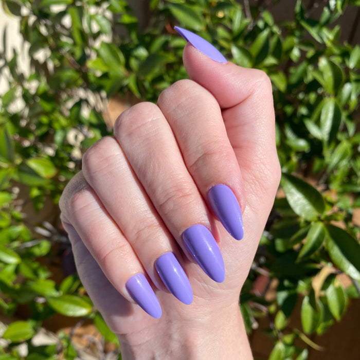 Bold & Unshaken - Press-On | Long | Almond showing hand with long almond press-on nails in vibrant purple polish outdoors