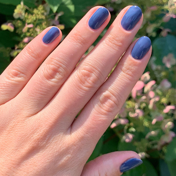 Hand with Social Studies nail polish in deep sun-bleached navy showing a glossy long-lasting manicure outdoors