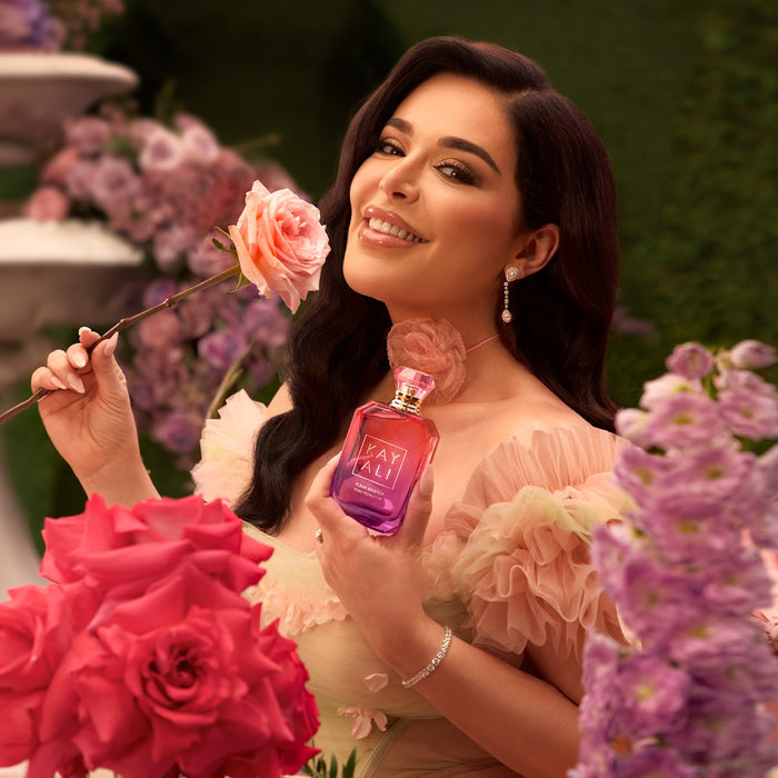 Mona Kattan holding a pink rose and Rose Royale perfume bottle with floral background
