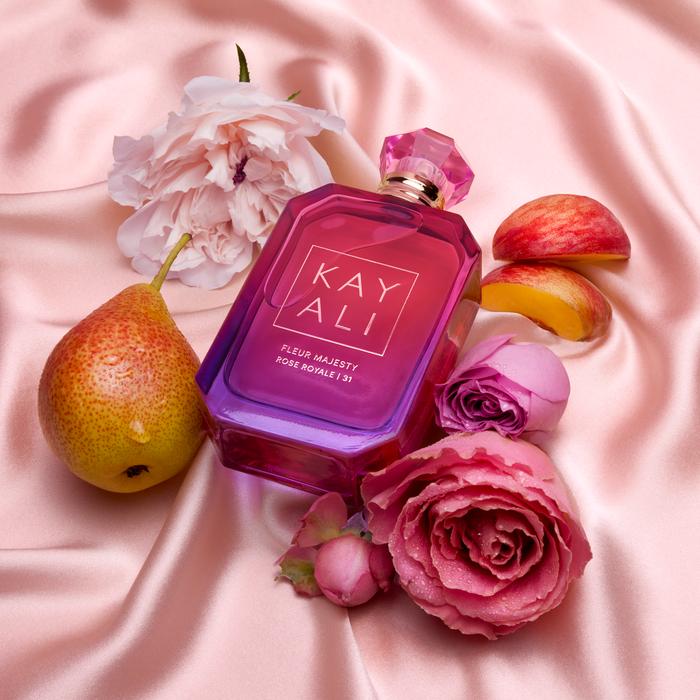 Rose Royale pink perfume bottle with flowers and fruits on a pink fabric background