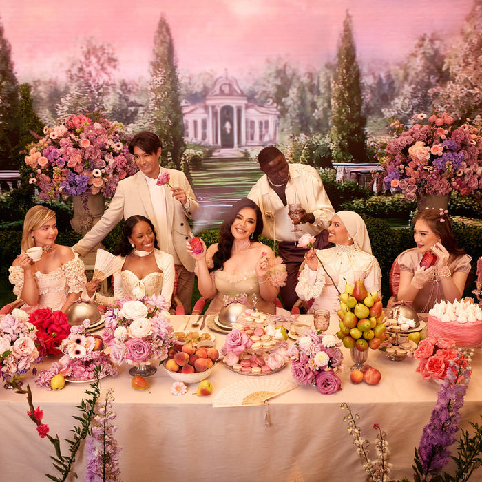 Group of people sitting at a table with floral decorations and desserts in an outdoor garden setting.