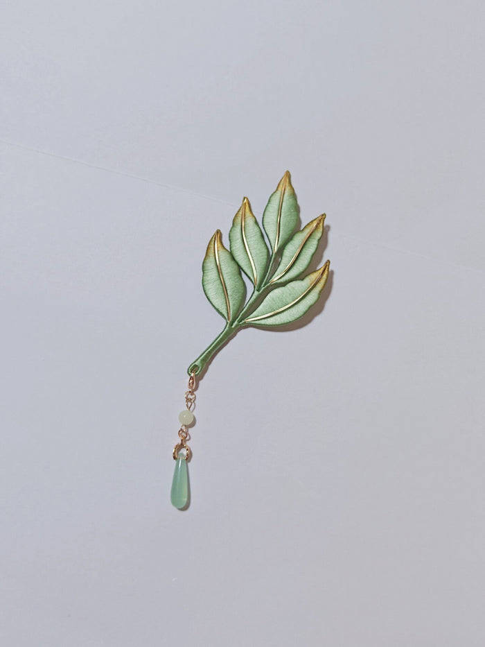 Chanhua handmade green leaf brooch with gold-trimmed edges and jade-green drop pendant on a gold chain, displayed on a light gray background