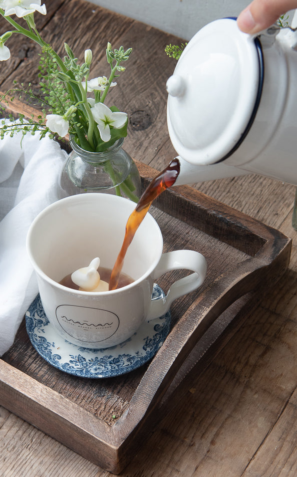 Person pouring coffee into a white mug with the round “Maman” logo and a bunny hidden inside.
