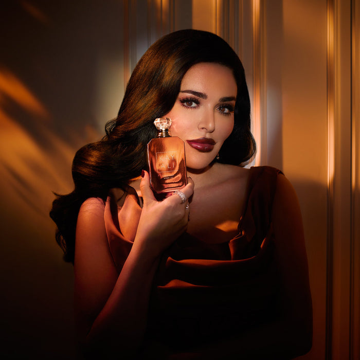 Woman holding a perfume bottle in a warm, dimly lit setting
