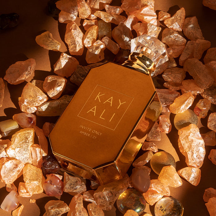 Gold perfume bottle with 'KAYALI' branding on a bed of amber-colored stones.