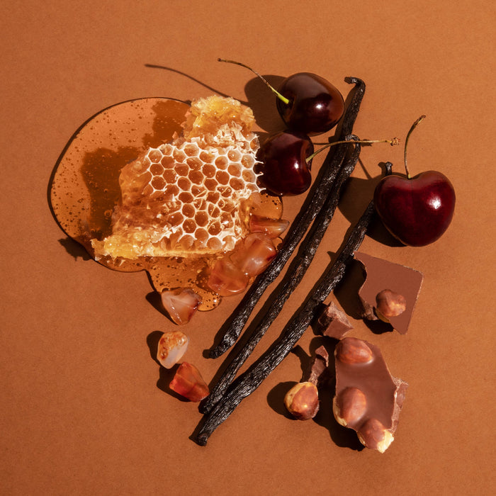 Honeycomb, cherries, vanilla beans, and chocolate on a brown background