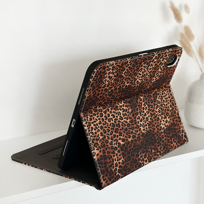 Leopard print iPad case on a white shelf next to a white vase filled with dried grasses.