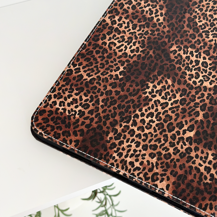 Leopard print iPad case on a white desk, with green leaves visible underneath.