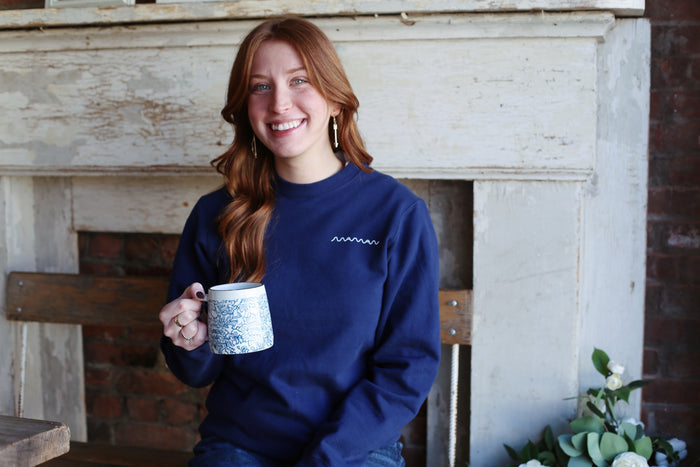 Person wearing a navy blue crewneck sweatshirt with the “maman” logo on the left chest.