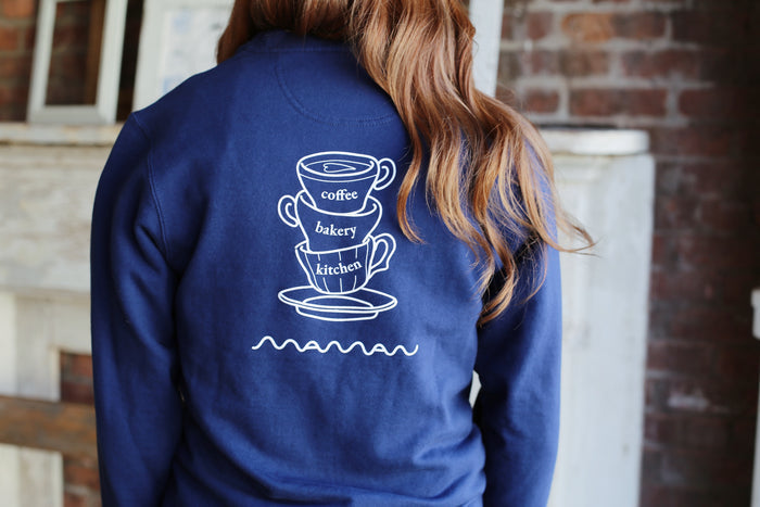 Back of the navy blue crewneck sweatshirt with the “maman” logo, a drawing of three coffee cups, and the words “coffee”, “bakery”, and “kitchen”.