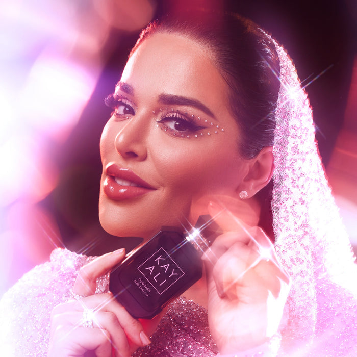 Woman holding a black bottle with 'KAYALI' branding against a blurred background