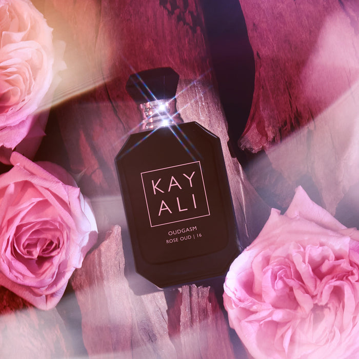 Perfume bottle labeled 'KAYALI' surrounded by pink roses on a textured background