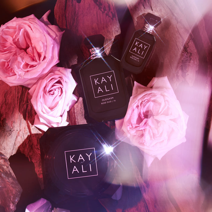 KAYALI perfume bottles surrounded by pink roses on a dark background