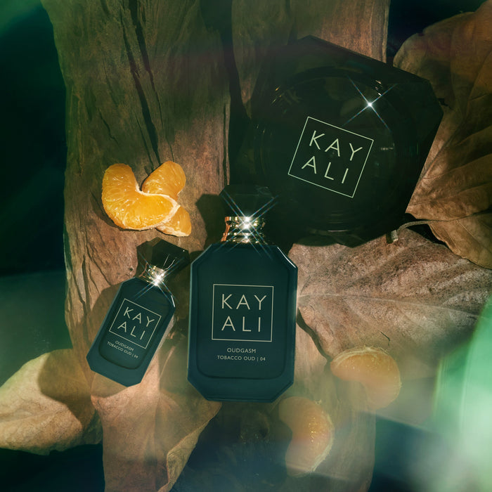 Three black perfume bottles with 'KAYALI' branding on a wooden surface with leaves and oranges.