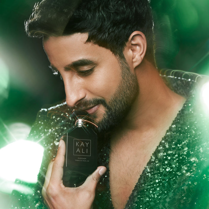 Man holding a black perfume bottle labeled 'KAYALI' with a green and white blurred background