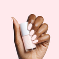 Hand with smooth nails painted in creamy pink PINK SANDS polish by Olive and June holding the bottle against pink background