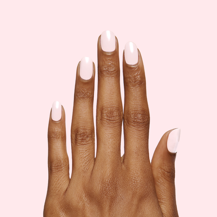 Hand with medium-length nails painted in soft pink PINK SANDS polish by Olive and June on pale background