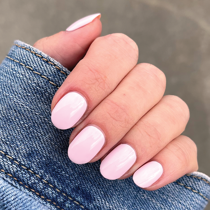 Hand with short nails coated in glossy PINK SANDS polish by Olive and June for a polished at-home mani look