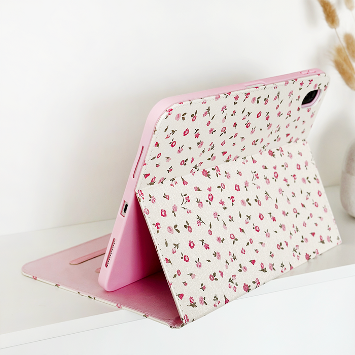Tablet in a pink watercolor floral iPad case on a white surface, with simple neutral decor in the background.