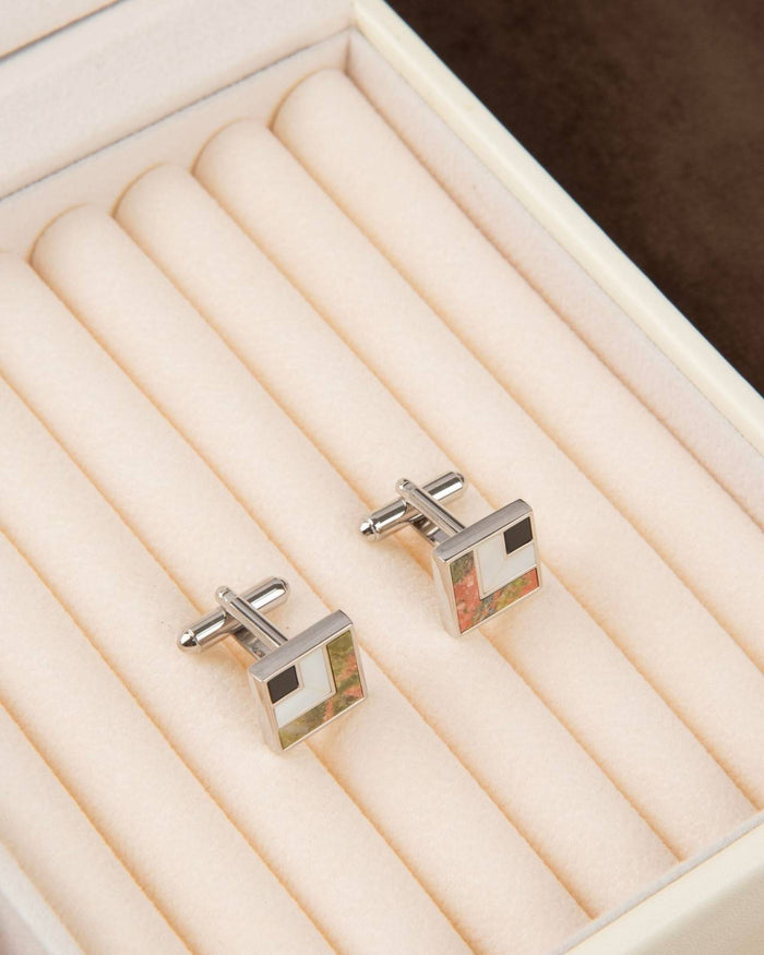 Square silver cufflinks with black enamel and multicolor abstract stone inlay on display.