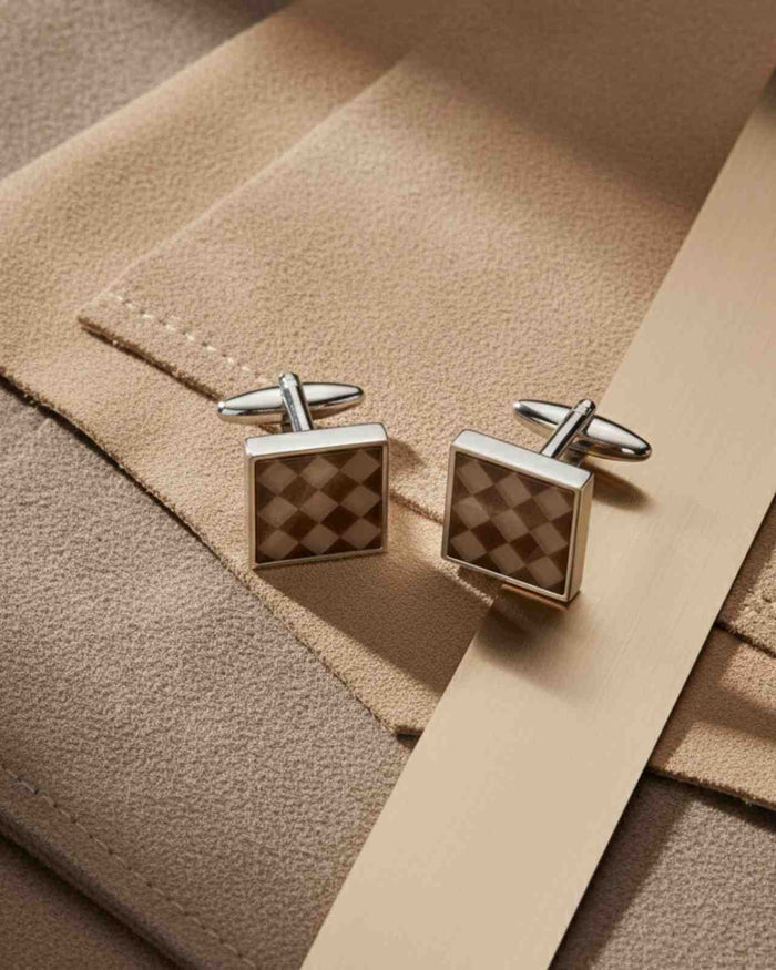 Square silver cufflinks with brown checkerboard inlay, on beige cloth