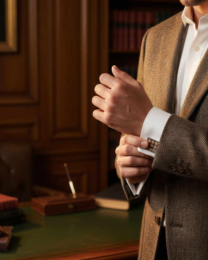 Square silver cufflinks with brown checkerboard inlay on shirt cuff