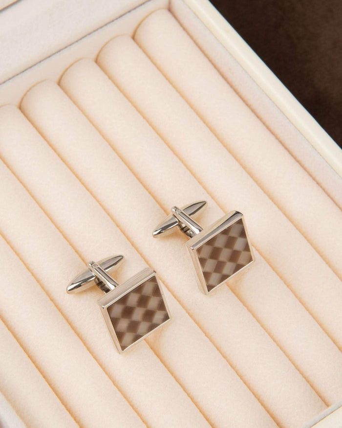 Square silver cufflinks with brown checkerboard inlay on a light display tray