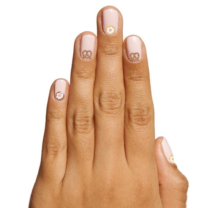 Hand with light pink manicure featuring Snack Time nail art stickers of pretzels and sunny-side-up eggs by Olive and June