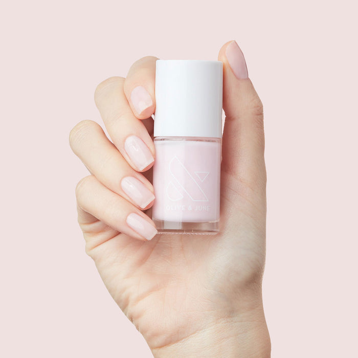 Hand holding bottle of Olive and June Strawberry Scone nail polish with nails painted in soft sheer pink manicure