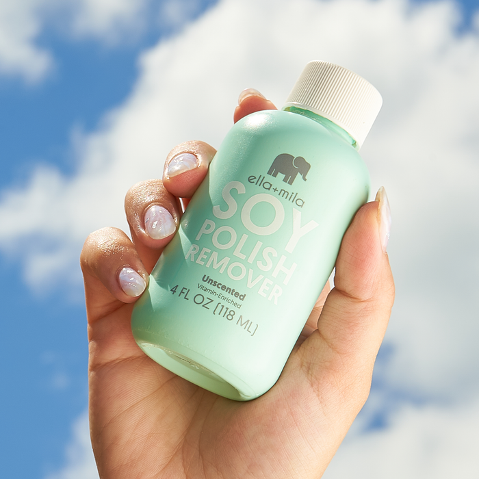 Hand holding Soy Nail Polish Remover unscented bottle against a blue sky