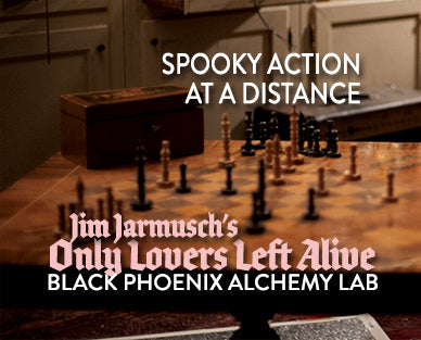Wooden chessboard with black pieces on a wooden floor, text overlay about 'Only Lovers Left Alive' and 'Black Phoenix Alchemy Lab'.