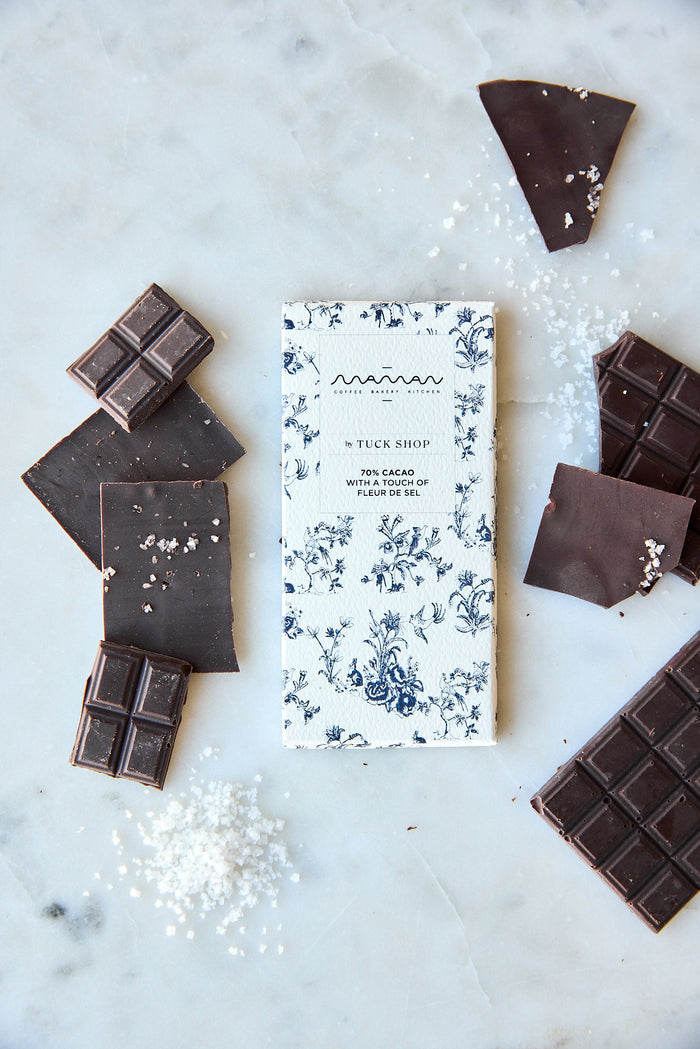 Chocolate bar surrounded by pieces of chocolate and sea salt, from the Tuck Shop x Maman collection with blue floral packaging.