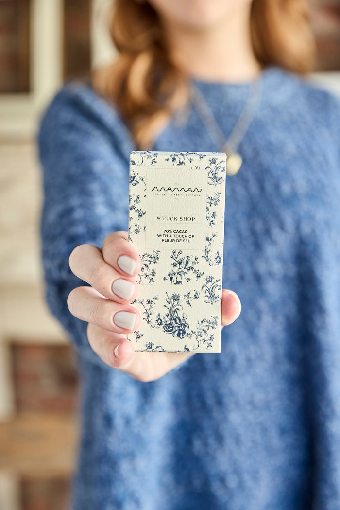 Person holding a chocolate bar with blue floral packaging from the Tuck Shop x Maman collection.