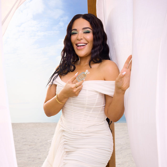 Mona Kattan in a white off-shoulder dress holding a microphone with a scenic background