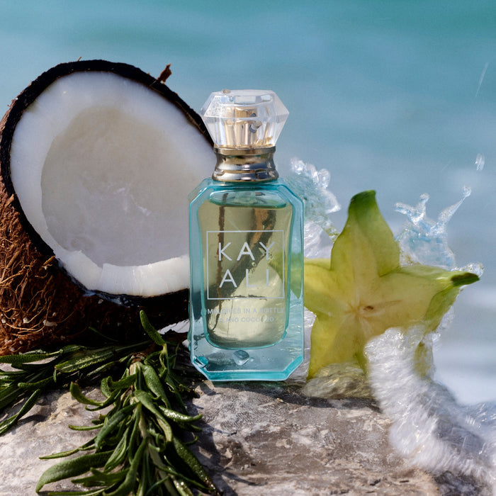 Perfume bottle labeled 'KAYALI' with a coconut, star fruit, and green leaves on a natural background