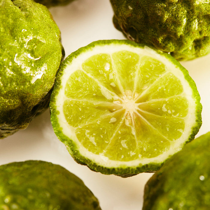 Close-up of a sliced green lime with whole limes around it on a white background