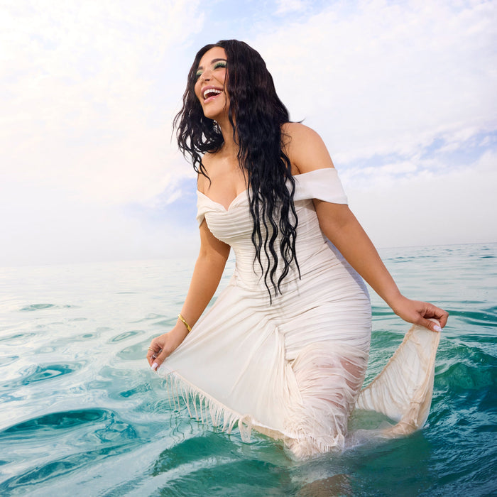 Mona Kattan in a white dress standing in water with a blue sky background