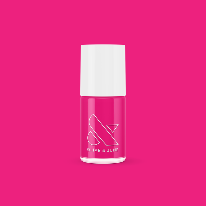 Bottle of Olive and June WILD ORCHID nail polish in rich magenta purple against a vibrant pink background