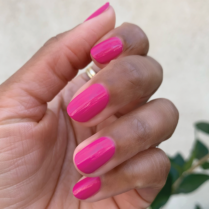 Hand with a smooth, glossy manicure in WILD ORCHID bright magenta polish against a neutral background